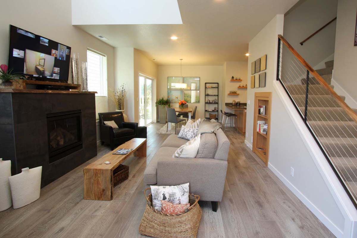 Open concept living area with fireplace, sectional sofa, dining area, kitchen bar, and modern cable-railed staircase.