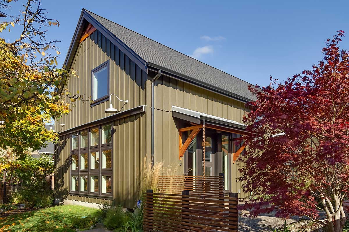 Modern house exterior with vertical siding, gabled roof, multiple windows, and a covered entrance with wooden supports.