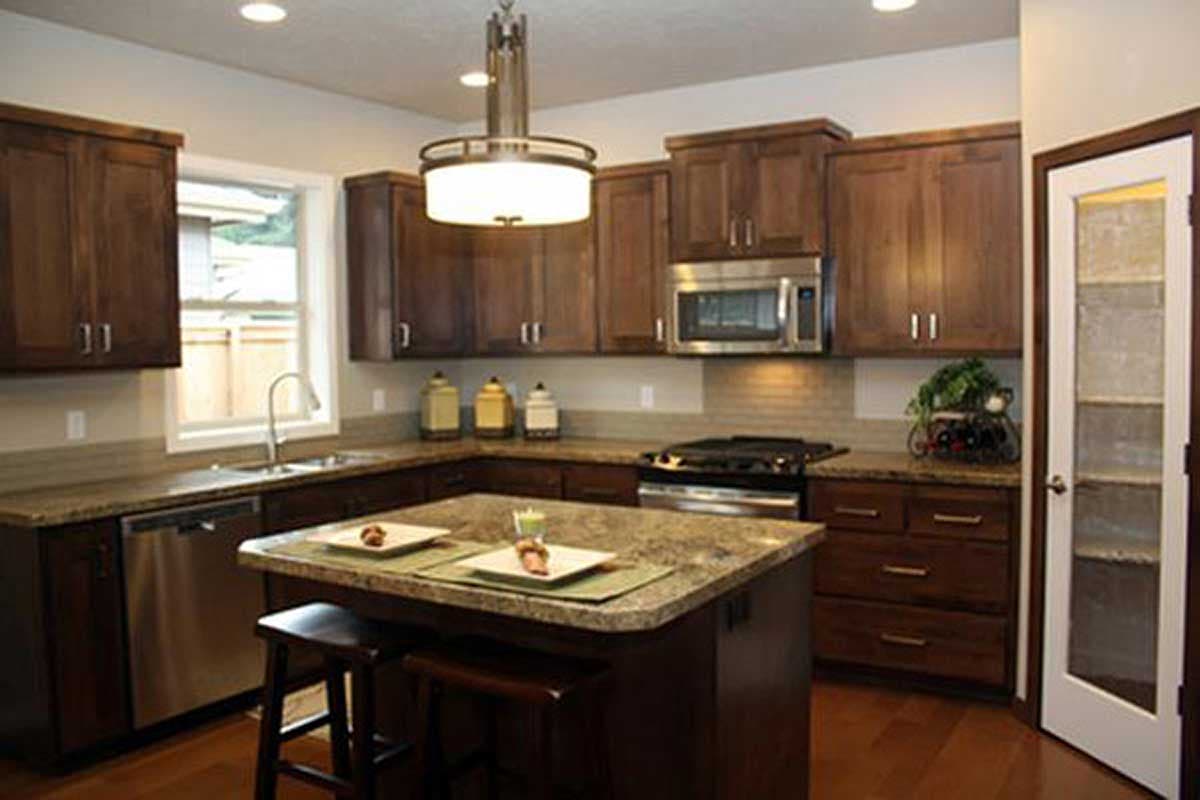 Kitchen with dark wood cabinets, granite countertops, island with seating, stainless steel appliances, and pantry door.