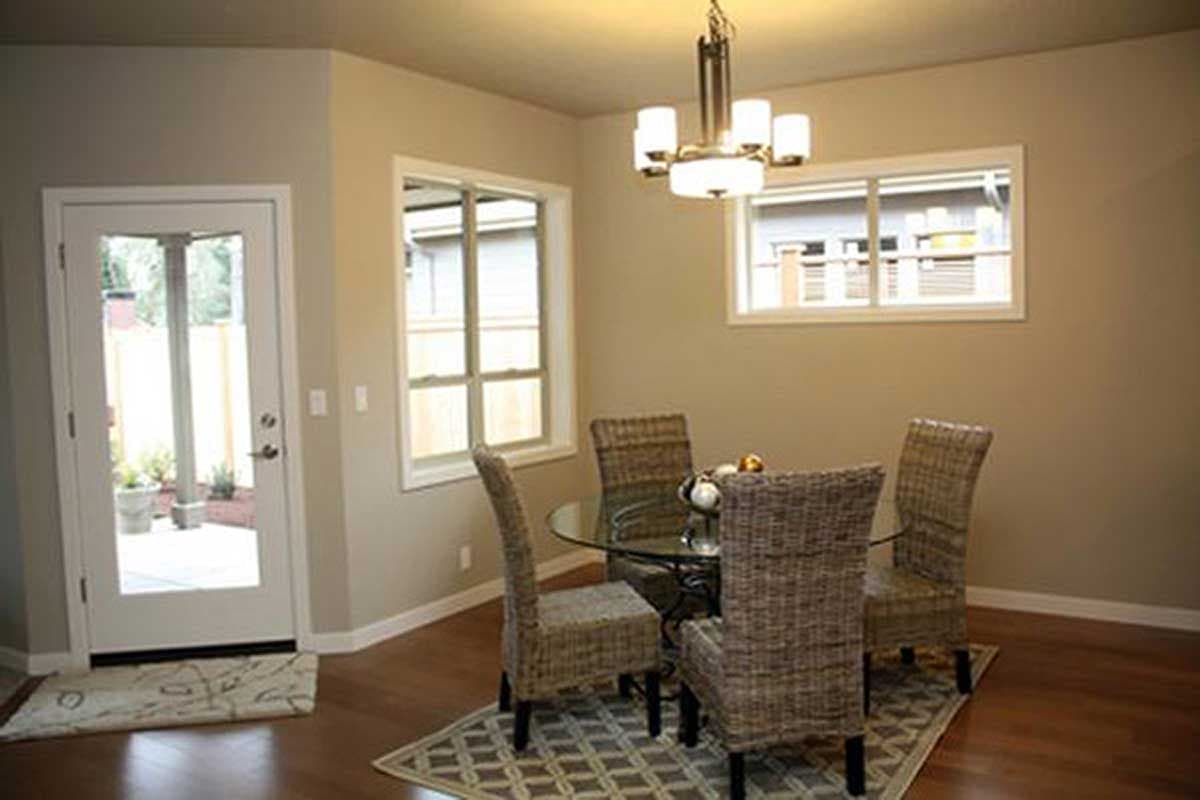 Dining room with glass-top table, four wicker chairs, a chandelier, two windows, and a glass door.
