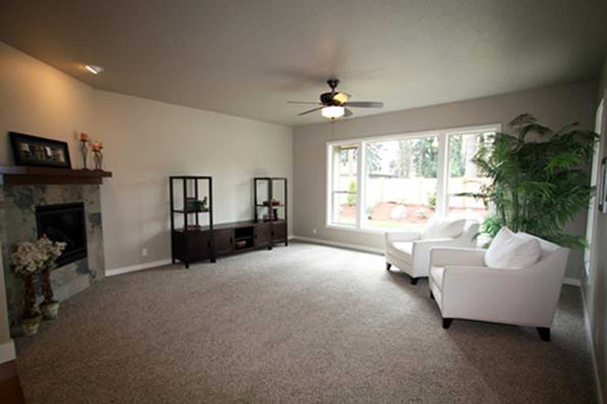 Living room with fireplace, media console, and large windows. Two white armchairs face the windows.