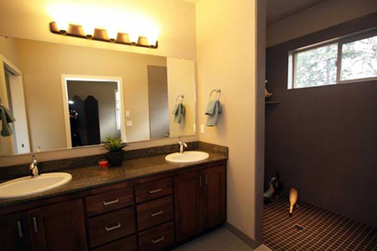 Bathroom with double vanity, dark wood cabinets, granite countertops, and a separate tiled shower with a horizontal window.