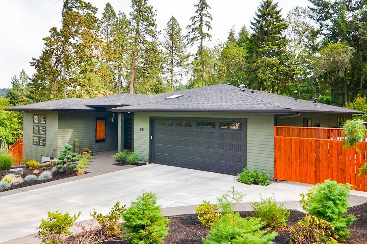 Modern ranch house plan exterior with green siding, prominent gable, attached garage, and orange wood fence.