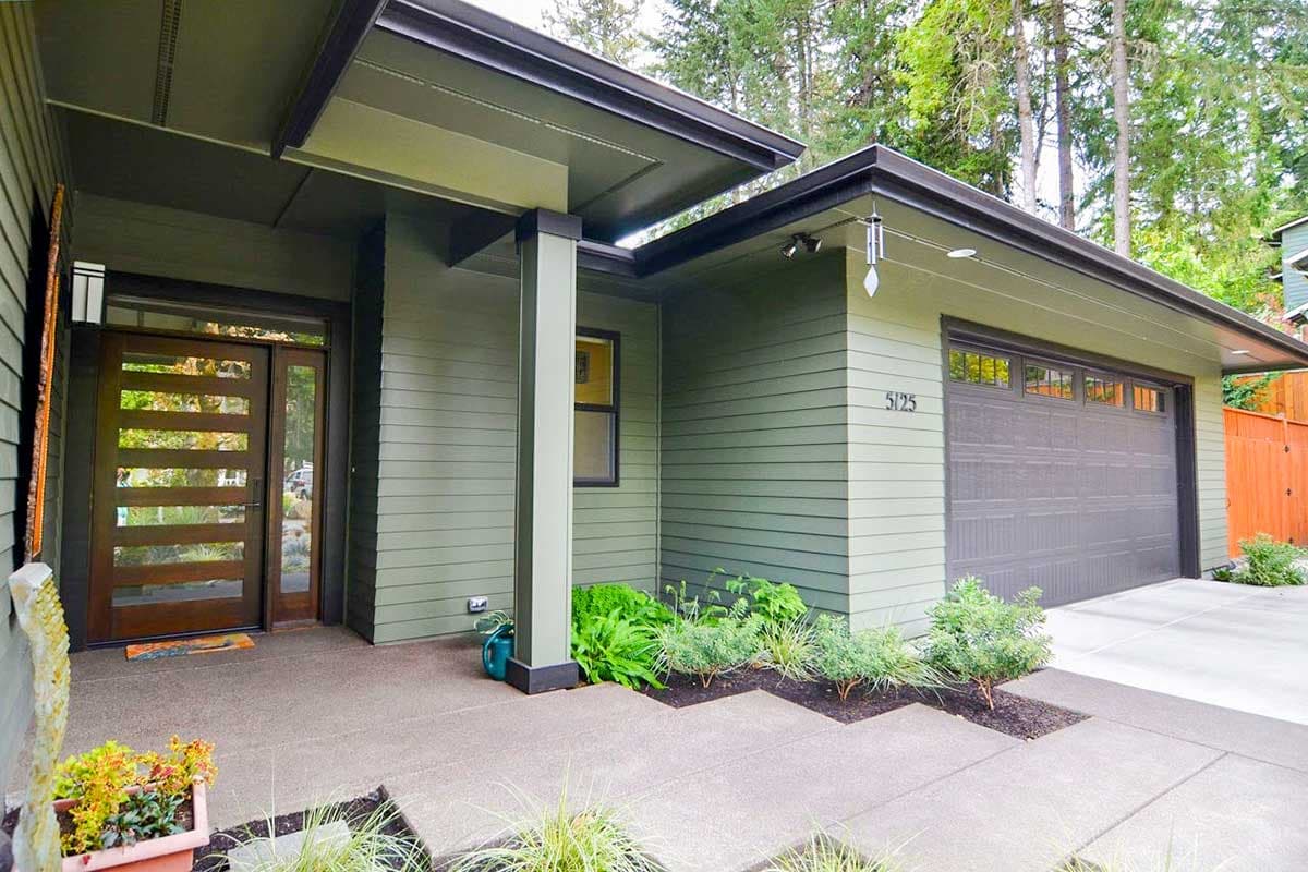Modern house exterior with horizontal siding, prominent overhangs, contemporary door, and attached garage.