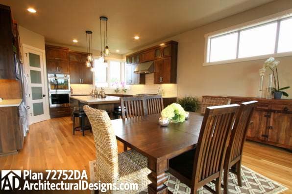 Dining area and kitchen interior with dark wood cabinetry, island, and pendant lighting. Plan 72752DA.