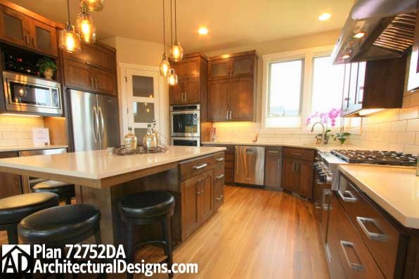 Kitchen interior with island, stainless steel appliances, wood cabinetry, and subway tile backsplash. Plan 72752DA.