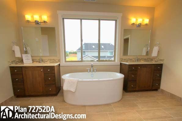 Bathroom with freestanding oval tub, double vanity, and large window with view of houses.