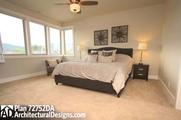 Primary bedroom with large corner windows, upholstered headboard, and ceiling fan. Plan 72752DA.