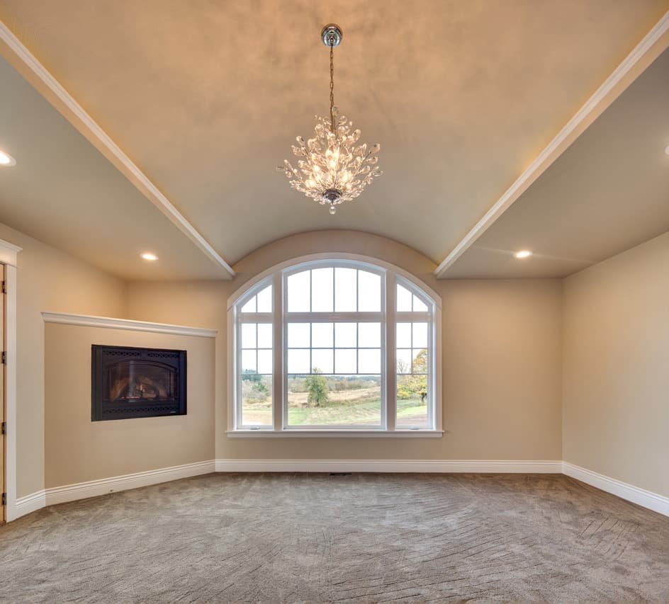 Interior view of a room with a fireplace, arched window, and vaulted ceiling with chandelier.