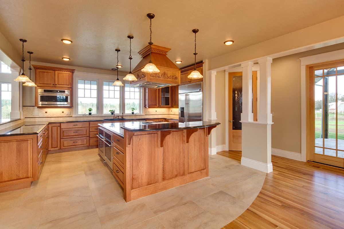 Kitchen with wood cabinetry, large island with black countertop, and windows overlooking the exterior.