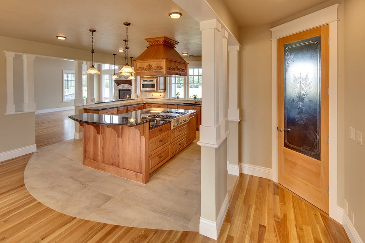 Kitchen with large island, range hood, fireplace visible in adjoining room, and interior door with decorative glass.