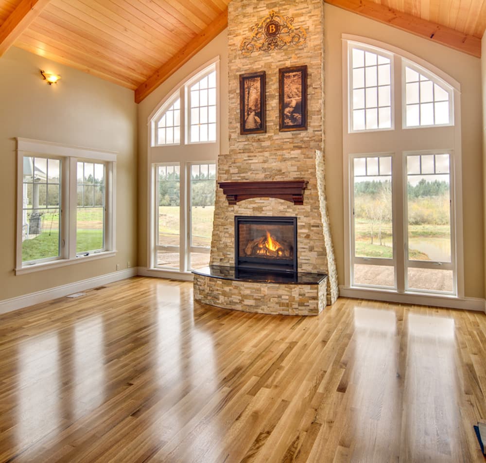Living room with stone fireplace, vaulted wood ceiling, large windows, and hardwood floors.
