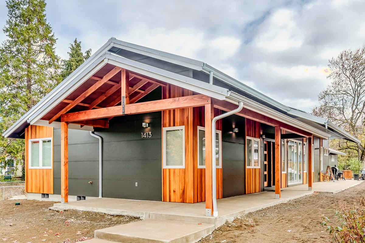 House plan exterior with a low-pitched roof, exposed wood beams, and a covered porch. Features both wood and dark-gray siding.