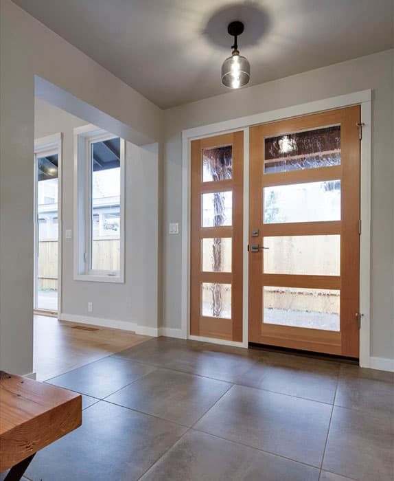 Interior view of a home entrance with double wooden doors featuring glass panels and a pendant light.