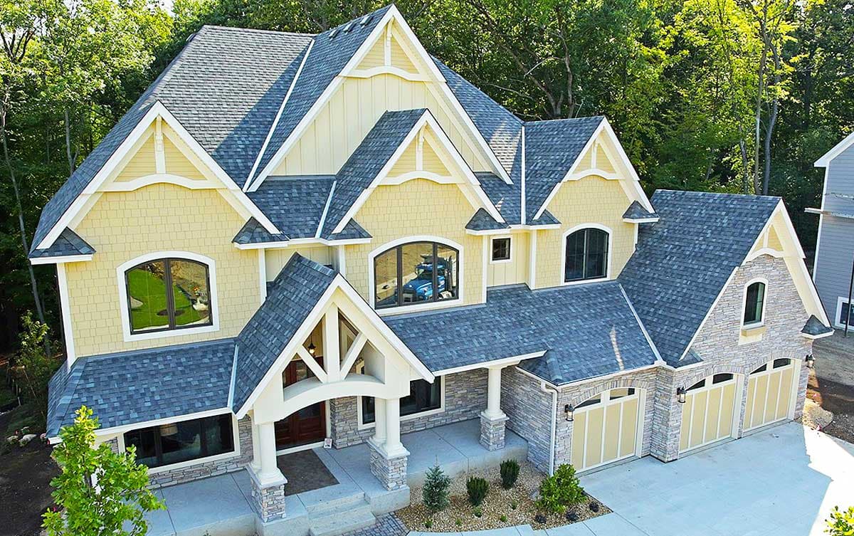 House plan exterior: Craftsman style, two stories, covered entry with stone pillars, multiple gables, stone and shingle siding, three-car garage.