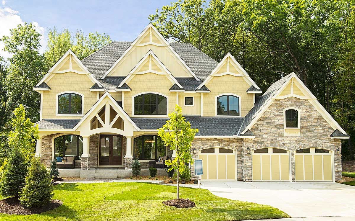 House plan exterior: Yellow siding, stone accents, arched windows, prominent gables, covered entry, three-car garage.