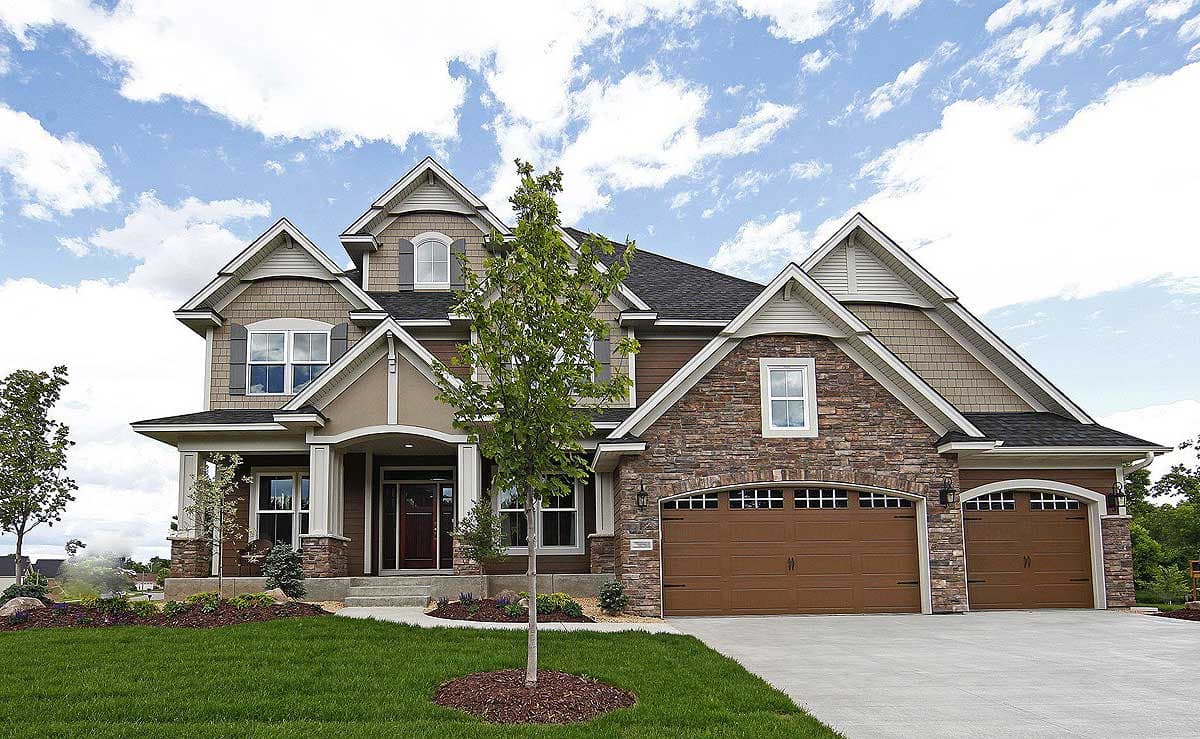 Exterior view of a two-story house plan with a stone facade, arched garage doors, multiple gables, and a covered entry.