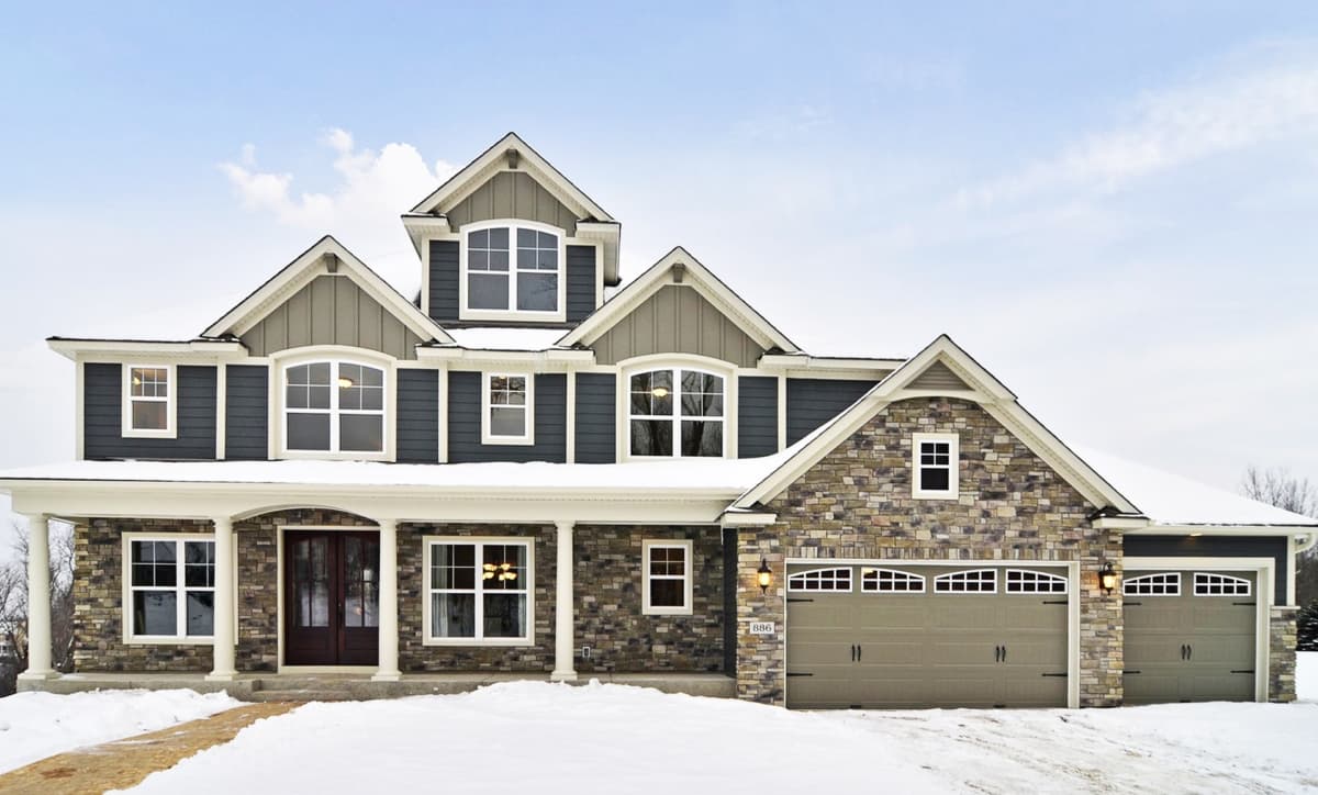 House plan exterior. Two-story home with a stone and siding facade. Features include a front porch, multiple gables, and an attached garage.