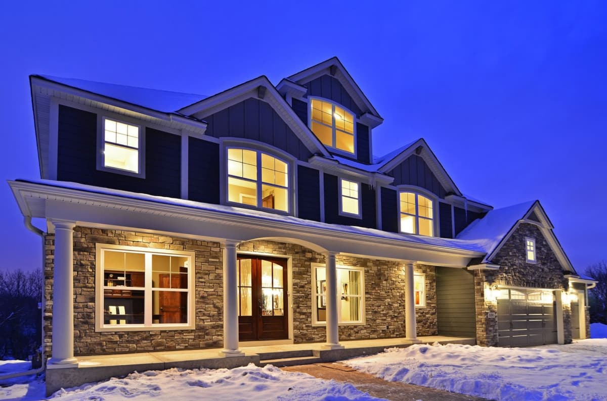 Two-story house plan exterior with stone facade, large covered porch with columns, multiple gables, and a side-entry garage.