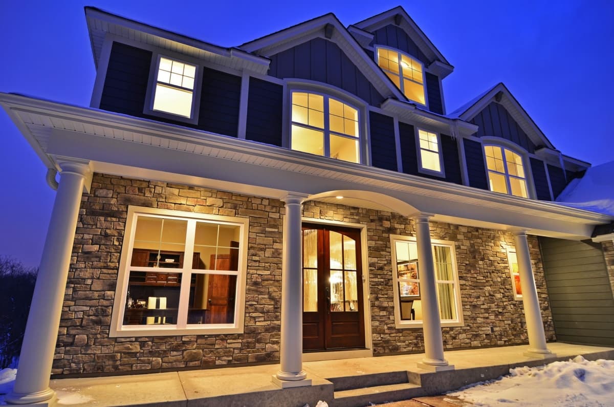 House plan exterior featuring stone facade, covered porch with columns, multiple gables, and numerous windows.