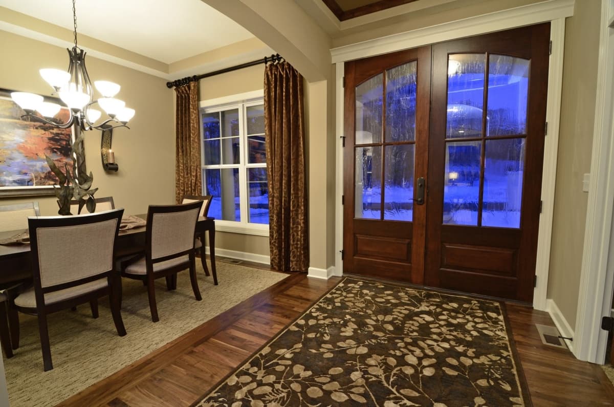 Interior view of a dining room with a table, chairs, window, and double wood doors with glass panes.