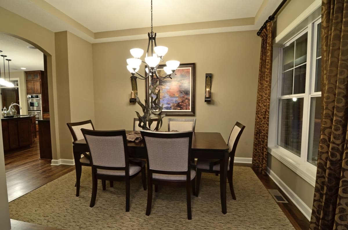 Dining room with dark wood table, upholstered chairs, chandelier, artwork, and large window with patterned curtains.