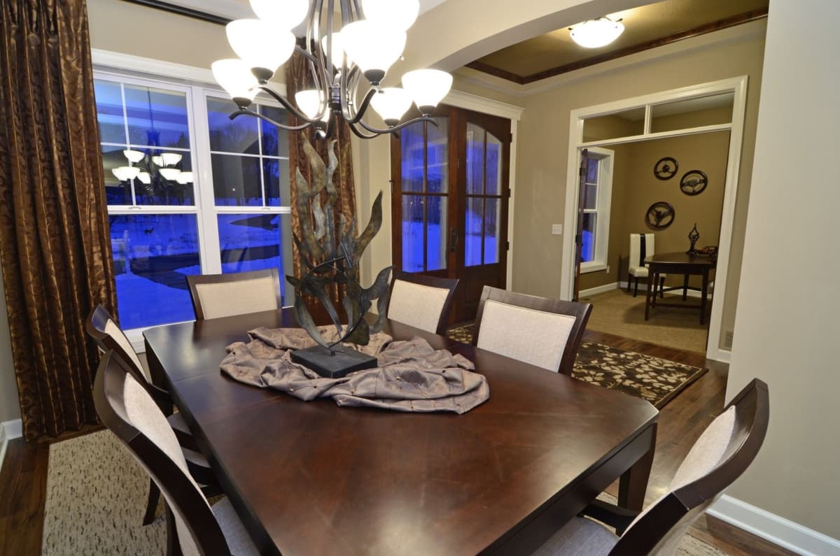 Dining room with dark wood table, upholstered chairs, large windows, and chandelier. Archway leads to a study.