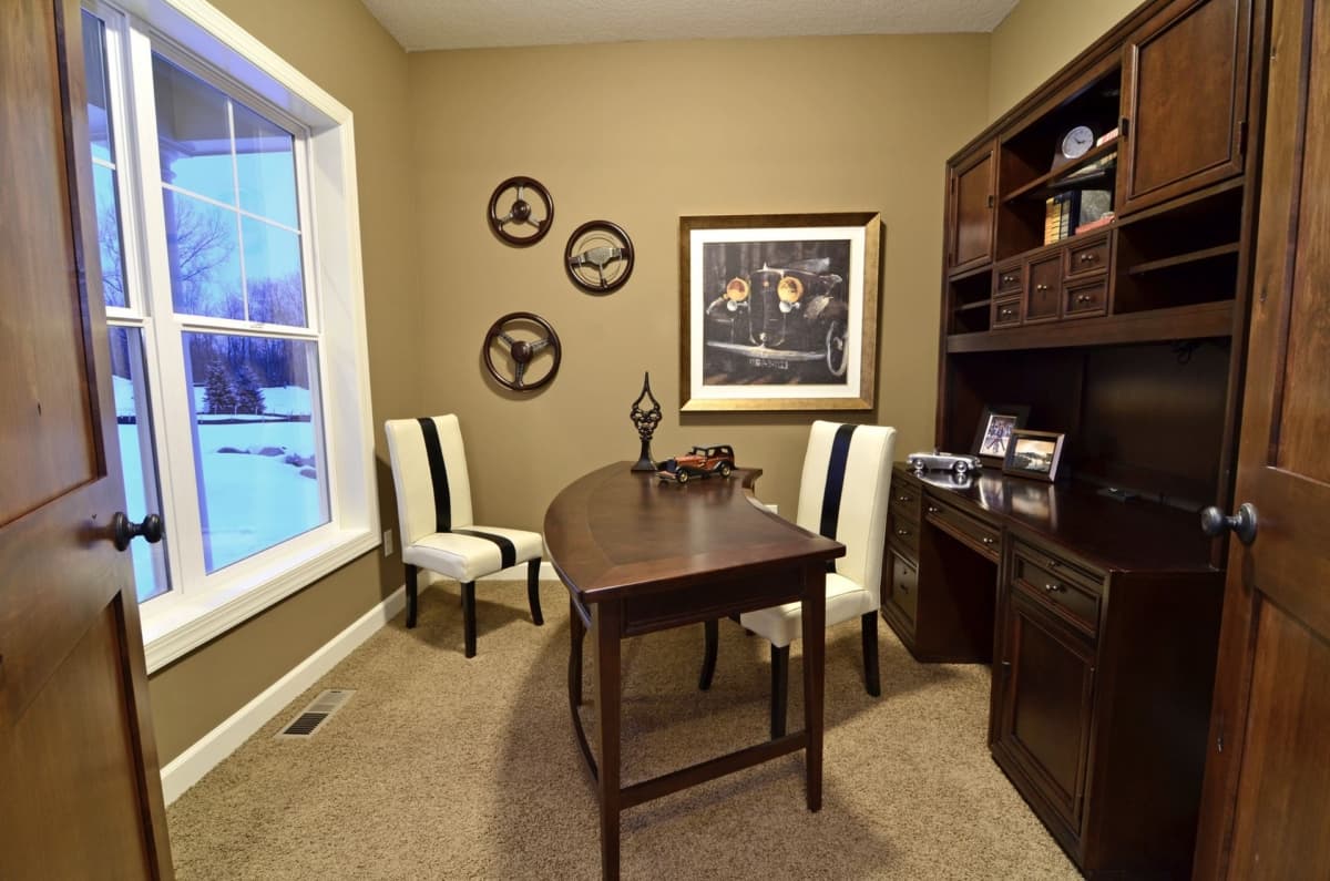 Home office with curved desk, built-in hutch, and vintage car art. Window overlooks a snowy landscape.