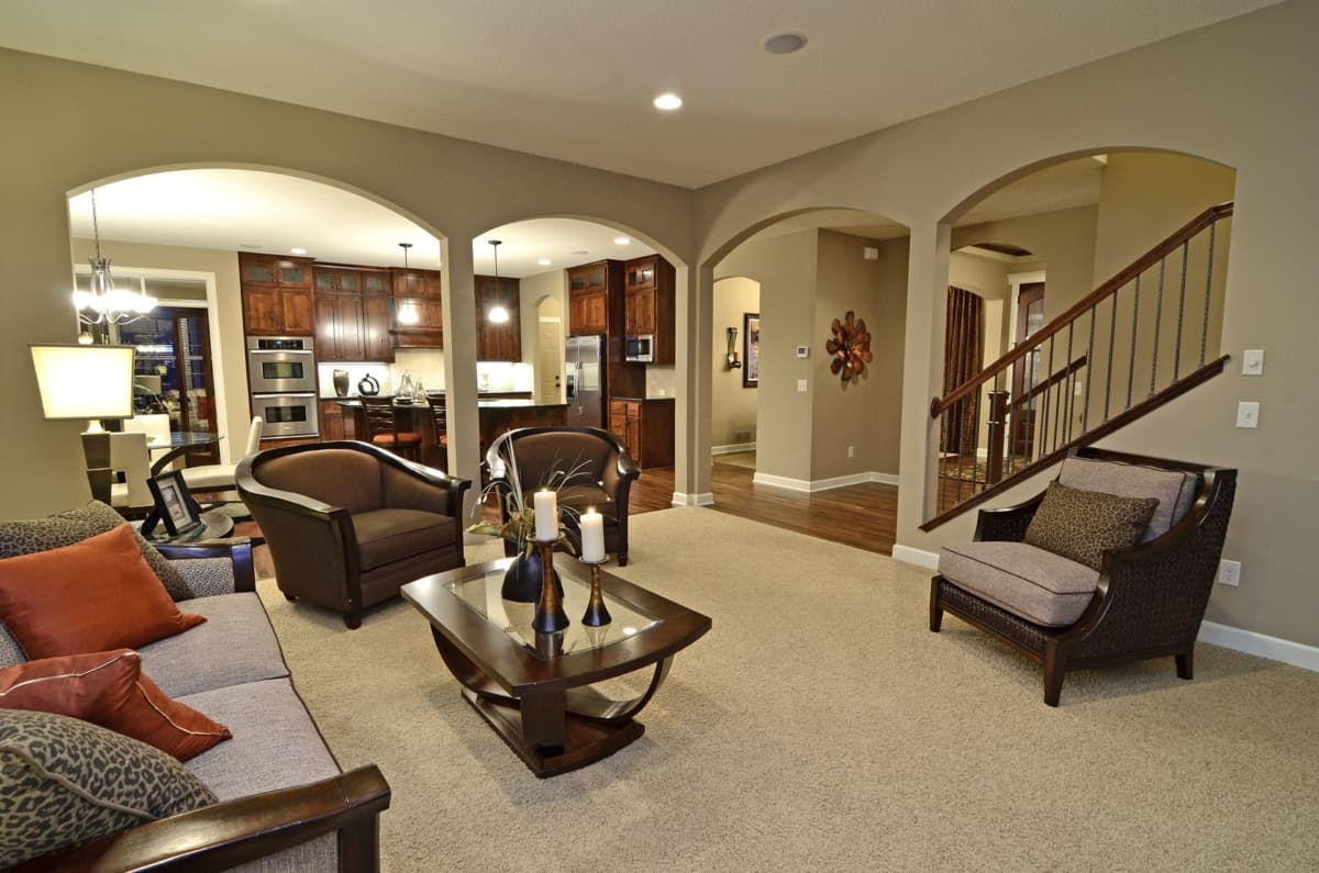 Interior view showing a living area with arched openings to a kitchen and a staircase, featuring furniture and cabinetry.
