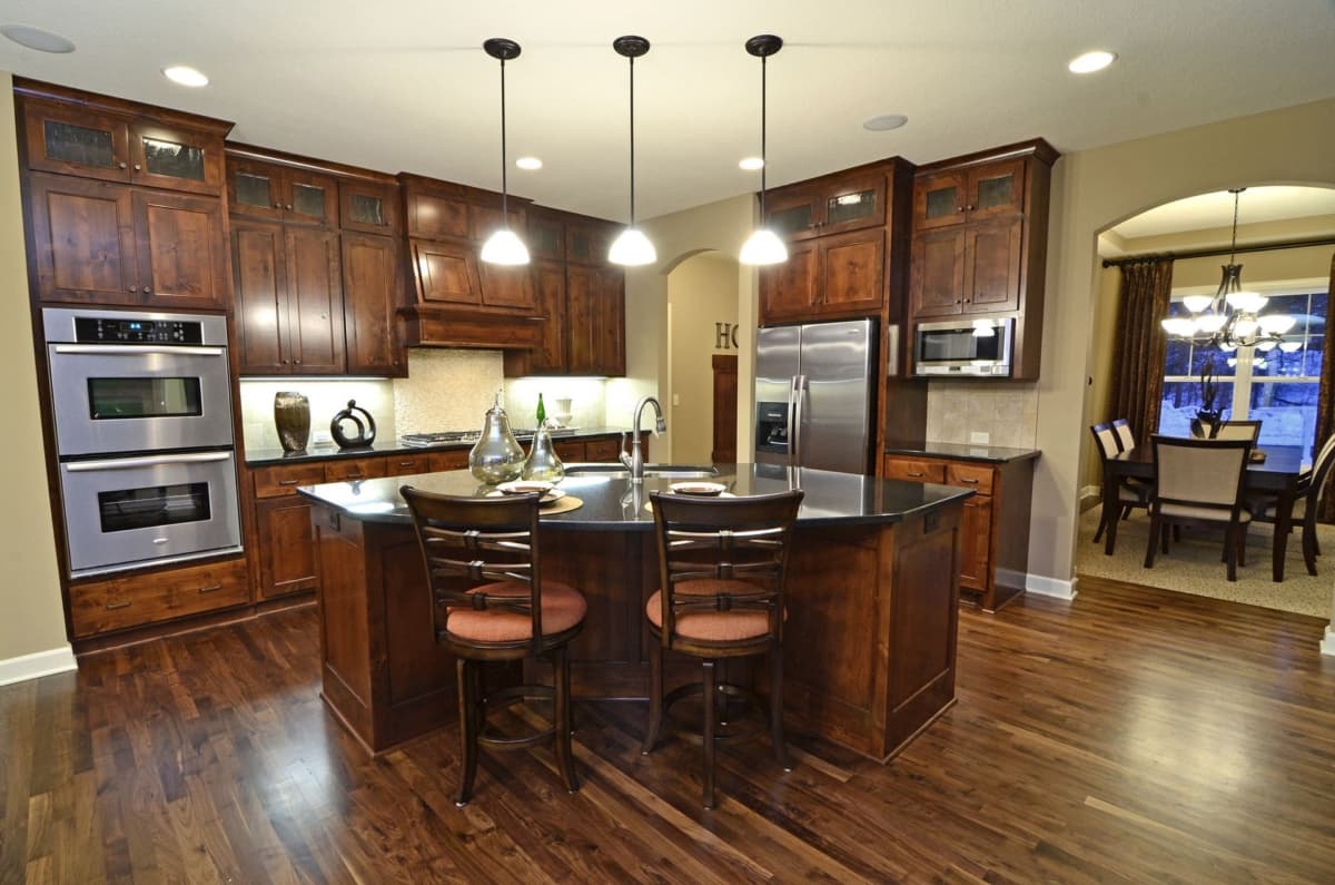 Kitchen with dark wood cabinetry, stainless steel double ovens, island with seating, and adjoining dining area.