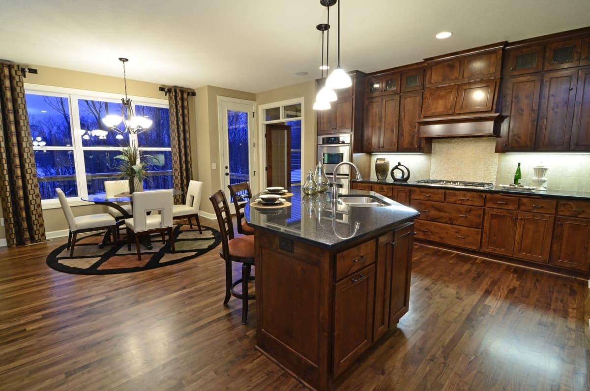 Kitchen with island, dining area, dark wood cabinets, granite countertops, stainless steel appliances, and large windows.