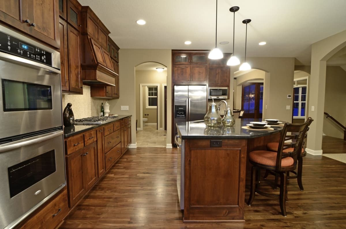 Kitchen with dark wood cabinets, granite island, stainless steel appliances including double oven, and pendant lighting.