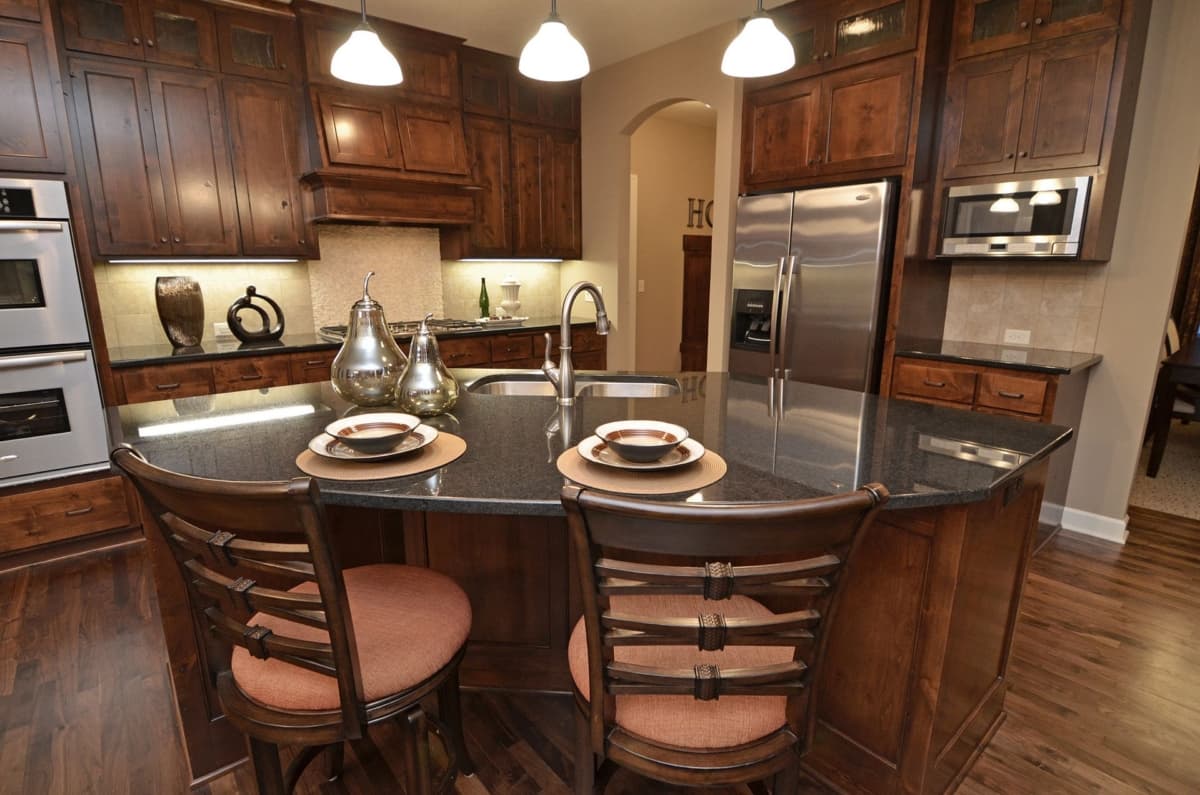 Kitchen with dark wood cabinets, granite island with seating, stainless steel double oven and refrigerator.