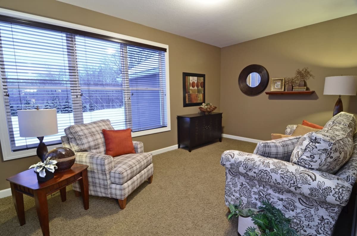 Living room with two armchairs, a dark wood cabinet, and large windows with blinds.