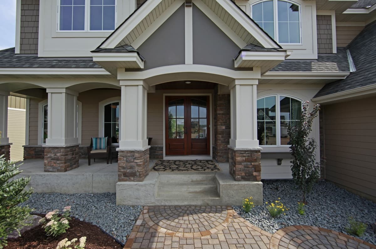 House plan exterior with covered porch, stone accents, double entry doors, arched windows, and layered rooflines.