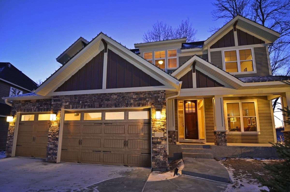 House plan exterior: Two-story home with stone accents, three-car garage, covered entry, and multiple gables.