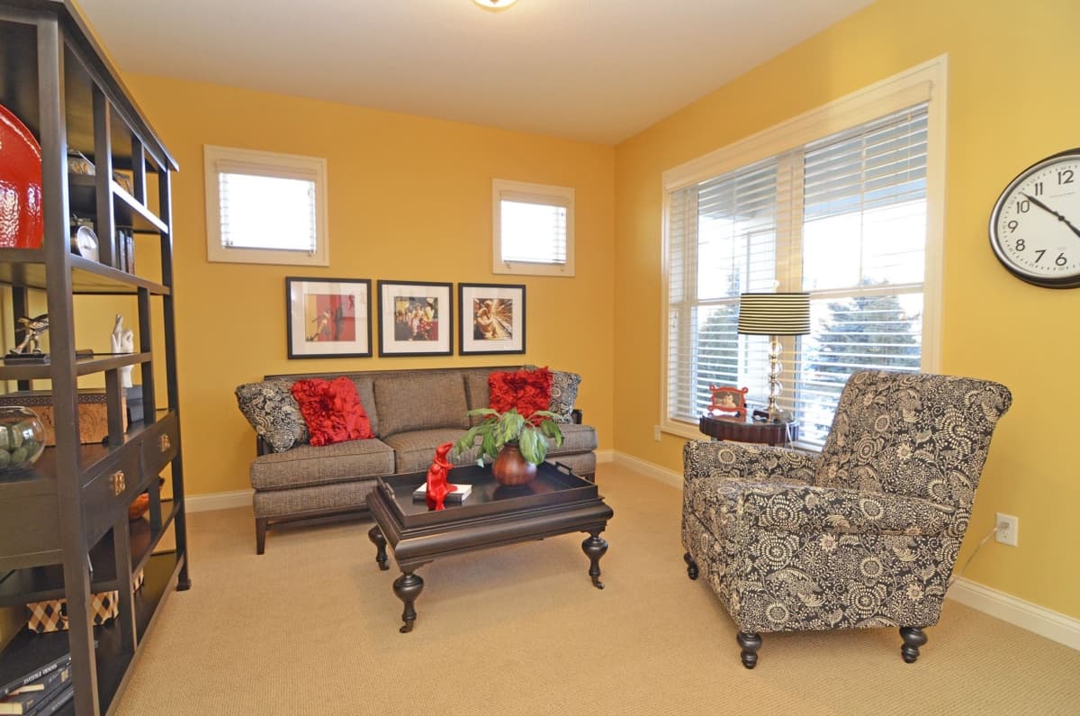 Living room with a sofa, armchair, coffee table, shelving unit, and framed artwork on yellow walls.