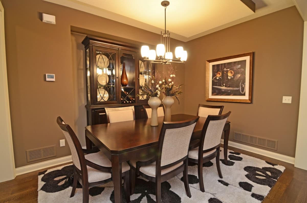 Dining room with dark wood table and chairs, glass-fronted hutch, modern chandelier, and framed artwork.