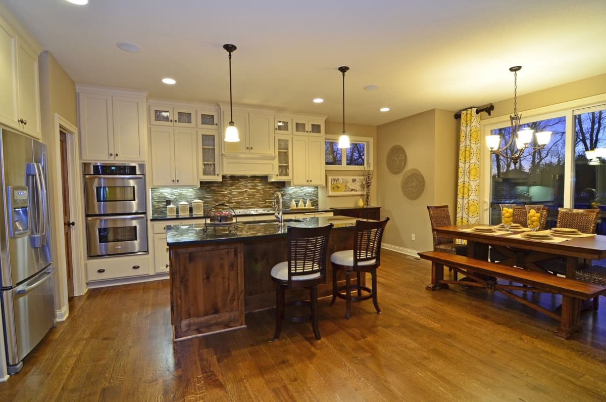 Kitchen and dining area featuring an island with seating, double ovens, dark wood cabinets, and a wooden dining set with bench seating.