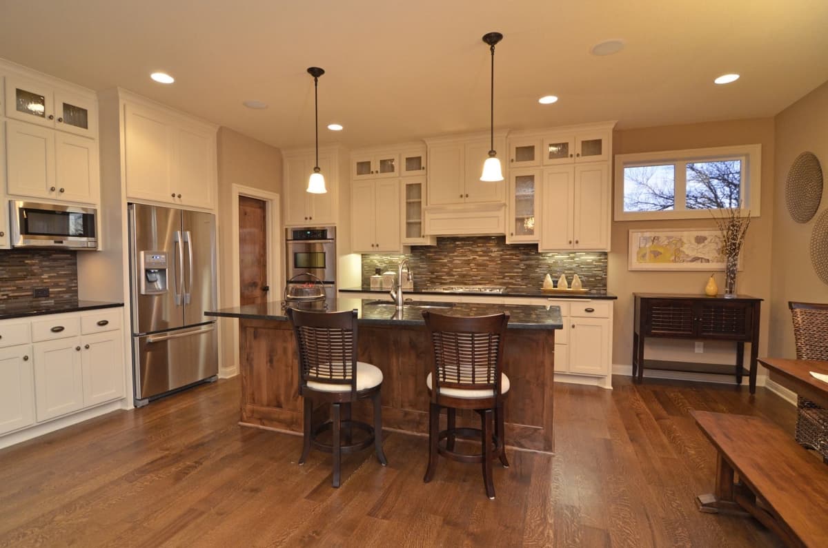 Kitchen interior with white cabinets, stainless steel appliances, island with seating, and hardwood floors.
