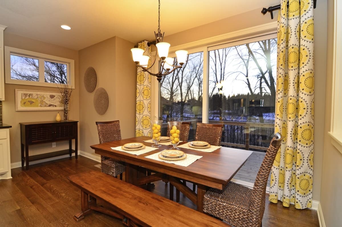 Dining room interior with wooden table set for four, bench seating, and large sliding glass doors overlooking a backyard with trees.