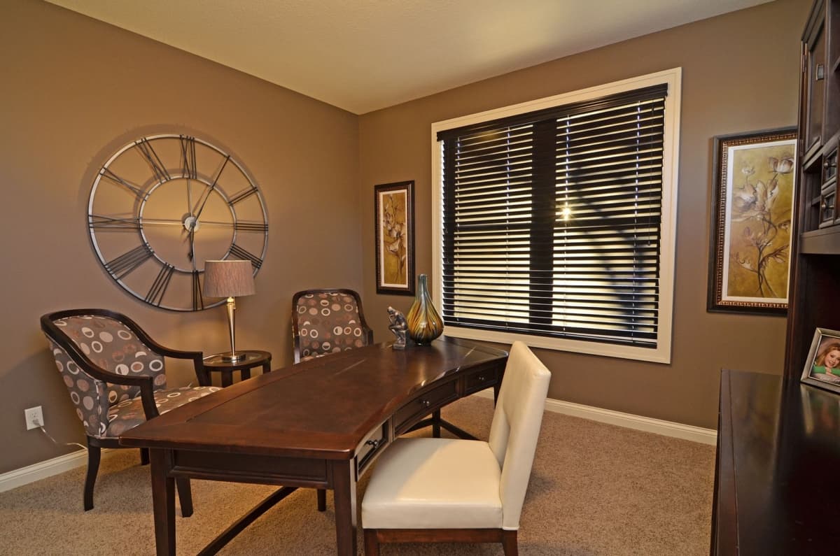 Office with dark wood desk, two patterned chairs, a large wall clock, and a window with blinds.