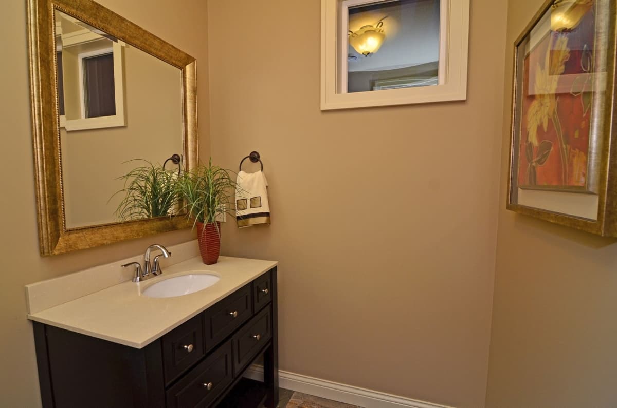 Powder room vanity with dark wood cabinet, quartz countertop, oval sink, large gold-framed mirror, and decorative wall art.