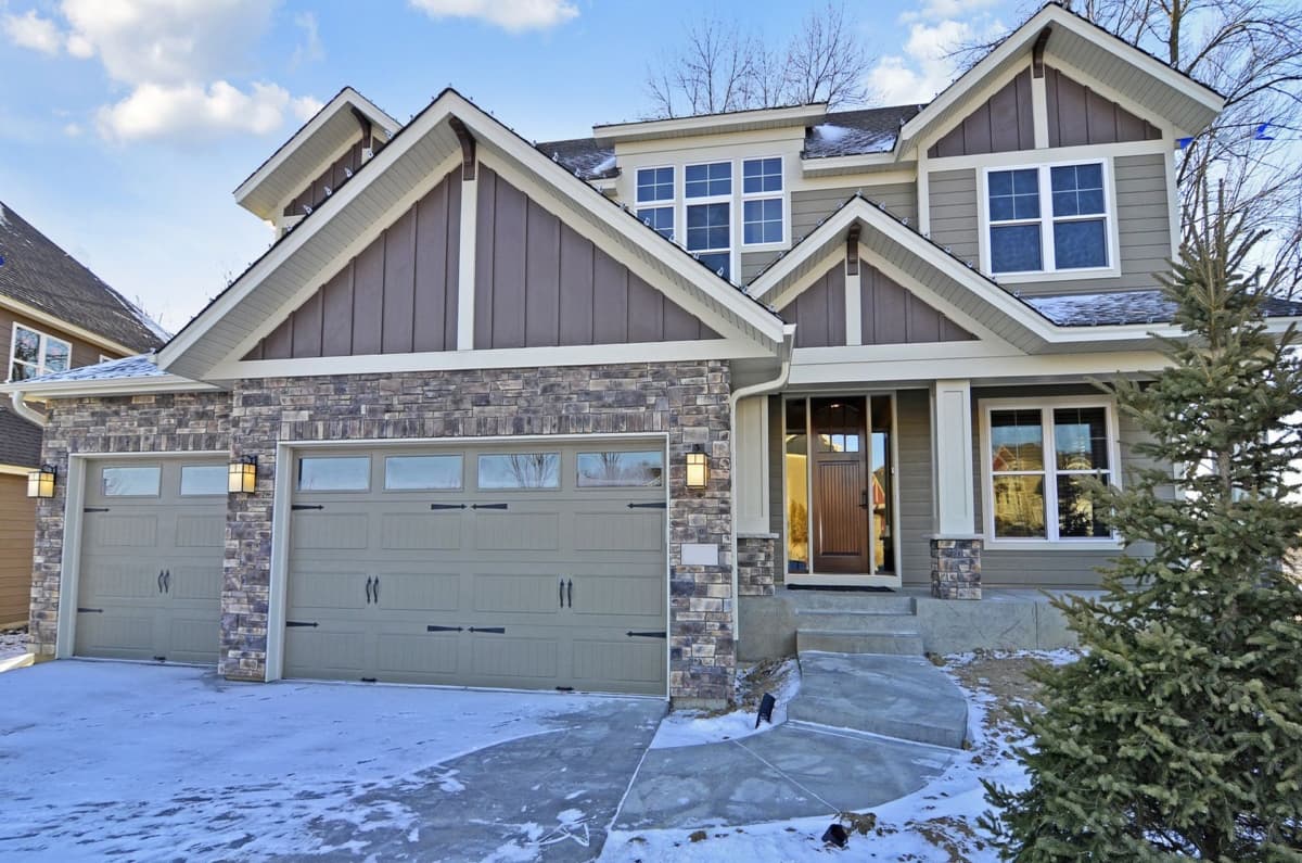 House plan exterior. Two-story Modern Farmhouse with stone facade, multiple gables, and a two-car garage. Features a covered entry and dormers.