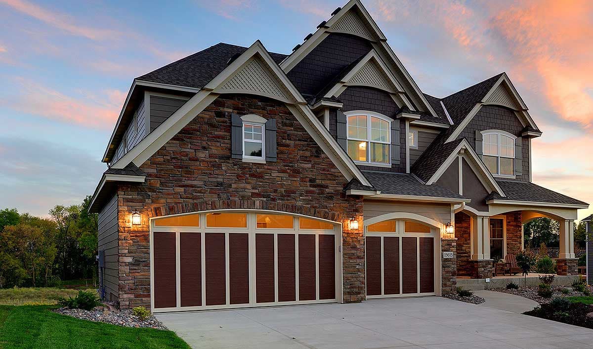 House plan exterior: Two-story home with stone accents, multiple gables, arched garage doors, and a covered front porch.