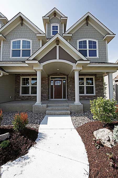 House plan exterior: Two-story home with arched window dormers, stone facade, and covered entry with columns.