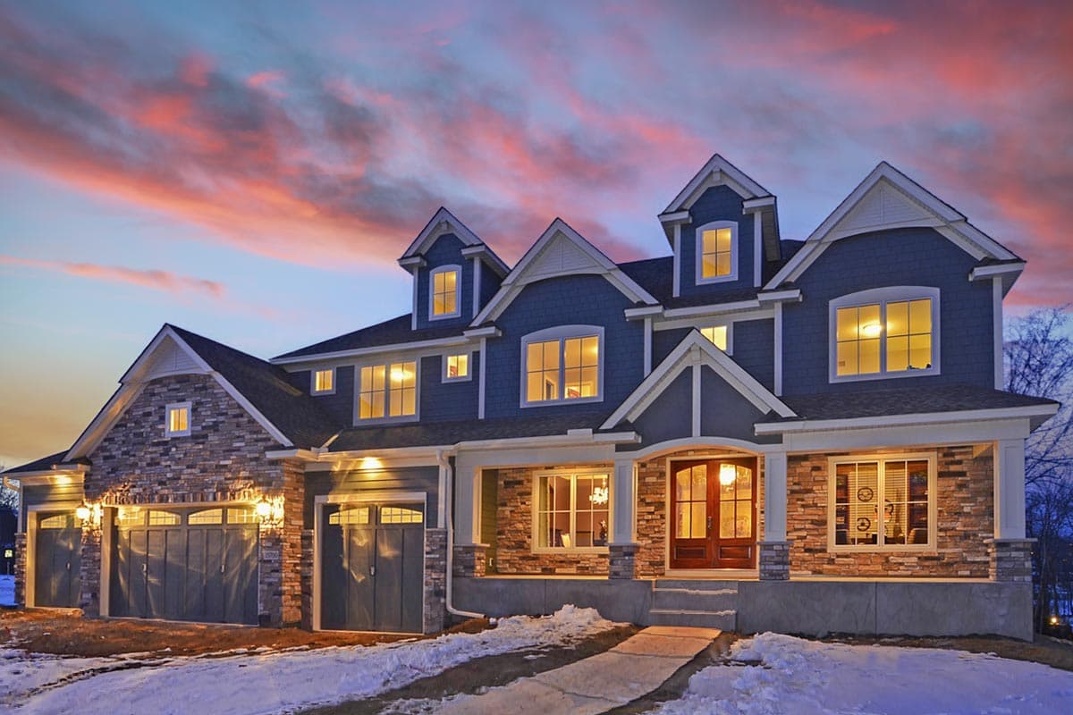 House plan exterior. Two-story home with Craftsman style. Features include a front porch, multiple dormers, stone facade, and a three-car garage.