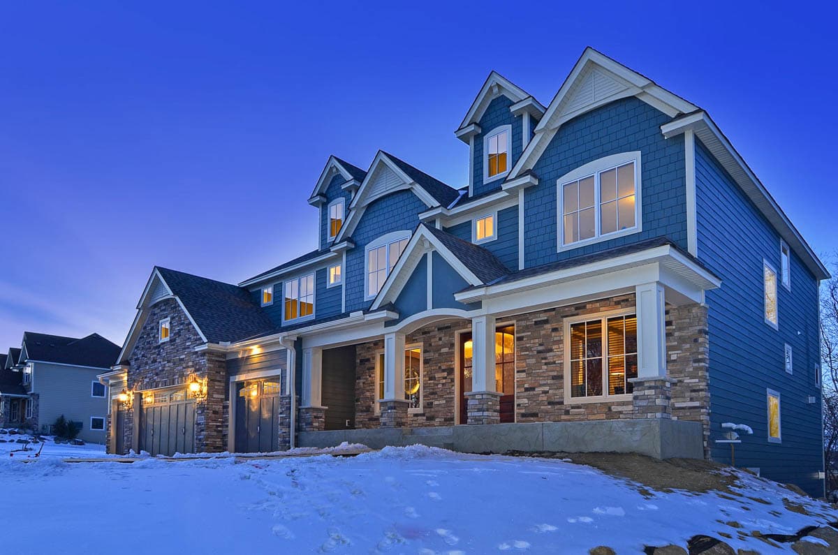 House plan exterior: Two-story blue home with stone accents, multiple gables, and a covered front porch.