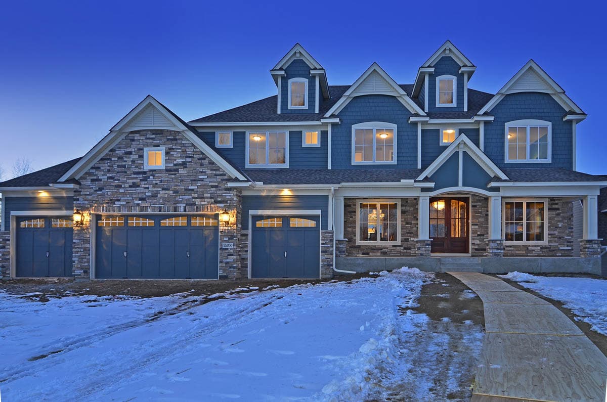 House plan exterior, two stories, blue siding, stone accents, multiple gables, dormers, and a three-car garage.