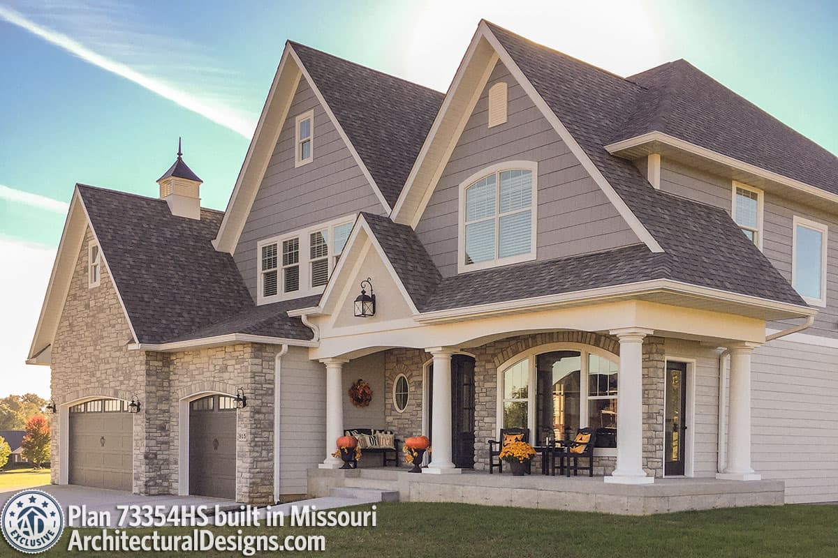 House plan exterior: two-story, stone and siding, gabled roof, covered front porch with columns, and a side-facing garage.